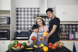 familia feliz tiene a papá, mamá y su pequeña hija cocinando juntos en la cocina foto