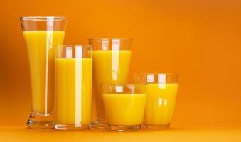 Glasses of orange juice isolated on colour orange background with copy space for text photo