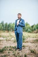 Guapo novio en traje de boda publicar en el parque foto