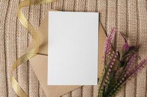A blank card is placed on an envelope with a ribbon, flowers and a sweater. photo