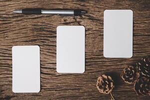 Three blank cards, a pen, and a dry pine cone are placed on top of the wood. photo