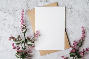 Se coloca una tarjeta en blanco con sobre y flor sobre fondo blanco. foto