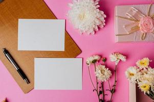 caja de regalo rosa, flor, bolígrafo, tablero de madera y tarjeta en blanco sobre fondo rosa foto