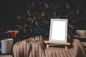 white photo frame on the stand and glasses on the sweater in classroom with cup and colored pencils.