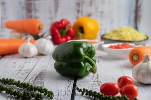 Bell peppers, fresh peppers, tomatoes, garlic and carrots on a white wooden background. photo