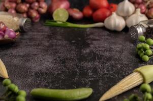 Baby corn, green peas, eggplant, garlic, tomato, lime, scallion and red onion placed on a black cement floor photo