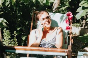 Woman laughing while making a phone call in a sunny garden during holidays, relax working from home
