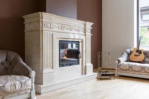 White marble fireplace in classic style with burning wood inside.