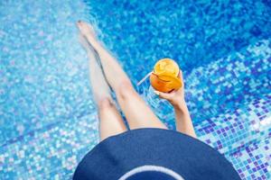 Woman in a blue hat relaxing at the pool with a  cocktail