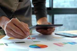 Hand businessman work on tablet in offices with graphs on the desk. photo