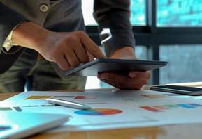 Hand businessman work on tablet in offices with graphs on the desk. photo