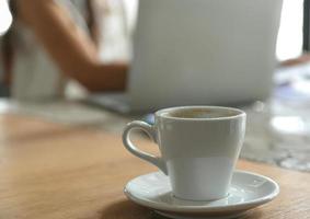 taza de café con leche en el escritorio con fondo borroso personas están usando laptop. foto