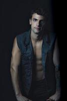 handsome man standing, looking at the camera, wearing a jean vest and naked torso. photo