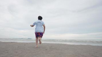 Chico lindo asiático corriendo felizmente en la playa con alegría video