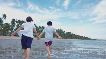 dois irmãos, um menino e uma menina da Ásia correndo alegremente na praia com alegria