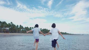 zwei Brüder, ein Junge und ein Mädchen aus Asien, die fröhlich am Strand laufen video