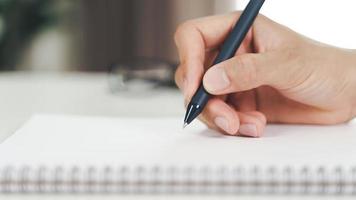 Close up of young man in casual cloth hands writing down on the notepad, notebook using ballpoint pen on the table. photo