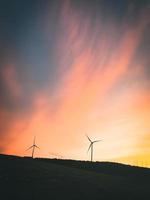 Wind turbines silhouettes in field aerial view bright orange sunset blue sky wind park slow motion drone turn. Silhouettes windmills, large orange dramatic sky with clouds. Sustainable energy photo