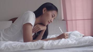 Aziatische vrouw met behulp van digitale tablet tekenen met een stylus pen afbeelding op slaapkamer thuis. video