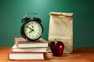 almuerzo, manzana, libros y reloj en el escritorio en la escuela. foto