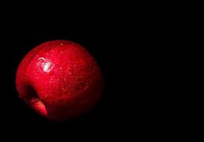 Gota de agua sobre la superficie brillante de la manzana roja sobre fondo negro foto