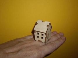 Pequeña casa de madera en la mano de un hombre sobre un fondo amarillo foto