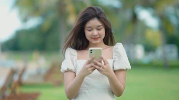 Aziatische schattig meisje ze gebruikt haar mobiele telefoon om met haar vrienden te praten met plezier. video