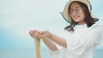 schattig Aziatisch meisje wandelen op het strand aan het strand. langzaam liet ze de zandkorrel uit haar hand los. video