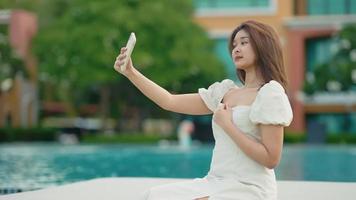 Linda chica asiática caminando por la playa, usó su teléfono celular para caminar tomando fotos de selfies video