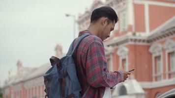 portret van knappe toeristen aziatische man die een smartphone gebruikt die kaart controleert terwijl hij naast de straat in thailand staat. video