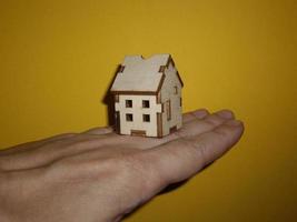 Pequeña casa de madera en la mano de un hombre sobre un fondo amarillo foto