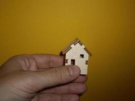 Pequeña casa de madera en la mano de un hombre sobre un fondo amarillo foto