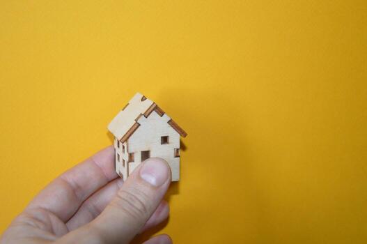 Small wooden house in a man's hand on a yellow background photo
