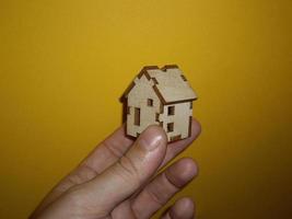 Small wooden house in a man's hand on a yellow background photo