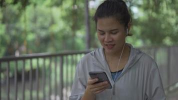 Corredor de fitness mujer asiática caminando y usando teléfono móvil escuchando música en un parque público.