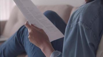 mujer asiática sosteniendo y leyendo documentos mientras está sentado en el sofá en la sala de estar en casa. video