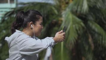 coureur de fitness femme asiatique debout à l'aide d'un téléphone portable écoutant de la musique dans un parc public. video