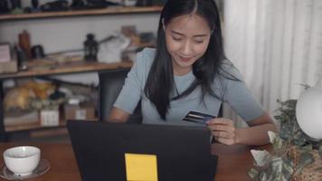 mujer asiática con tarjeta de crédito usando laptop comprando en línea en casa. video