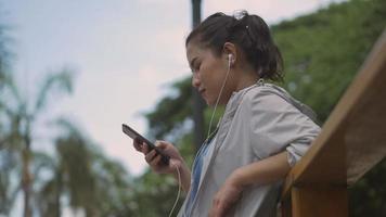 Corredor de fitness mujer asiática mediante teléfono móvil escuchando música en un parque público. video