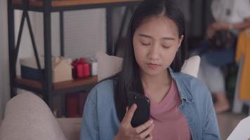 Asian woman talking on phone and reading documents while sitting sofa in the living room at home. video