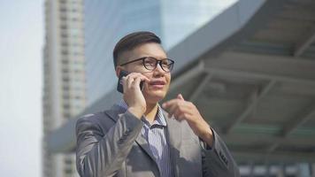 asiatisk affärsman talar telefon med en vän medan han går i stadsstaden. video