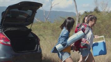 Las mujeres asiáticas ayudan a sostener mochilas y hieleras con amigos que acampan en la naturaleza durante un viaje de verano. video