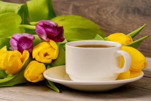 Tulipanes amarillos y púrpuras y taza de café en la mesa de madera rústica. fotografía de cerca. foto