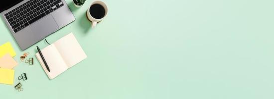 Creative flat lay of workspace desk. Top view office desk with laptop, coffee cup and open mockup black notebook on green background. Panoramic banner with copy space for text and Advertising area. photo