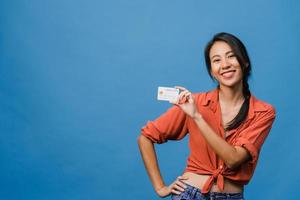 Young Asia lady show credit bank card with positive expression, smiles broadly, dressed in casual clothing feeling happiness and stand isolated on blue background. Facial expression concept. photo