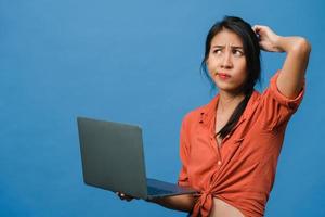 Jovencita asiática usando laptop con expresión negativa, gritando emocionado, llorando emocionalmente enojado en ropa casual y parado aislado sobre fondo azul con espacio de copia en blanco. concepto de expresión facial. foto