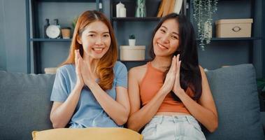Teenager couple Asian women feeling happy smiling and looking to camera while relax in living room at home. Cheerful Roommate ladies video call with friend and family, Lifestyle woman at home concept. photo