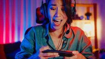 Happy Asia Girl Gamer Wear Concurso de auriculares Juega videojuegos en línea con luces de neón de colores para teléfonos inteligentes en la sala de estar de casa. juego de transmisión de deportes en línea, concepto de actividad de cuarentena en el hogar.