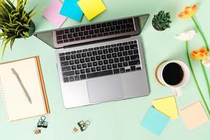 Creative flat lay photo of workspace desk. Top view office desk with laptop, coffee cup and open mockup black notebook on pastel green color background. Top view mock up with copy space photography.