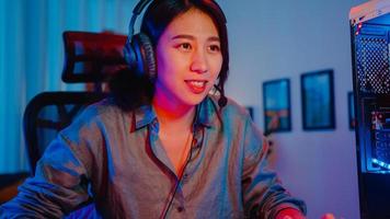 Happy asia professional girl gamer wear headphone participation play video game colorful neon lights computer in living room at home. Esport streaming game online, Home quarantine activity concept. photo